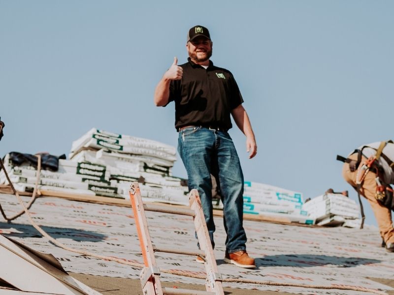 970 services roofer on a roof giving a thumbs up